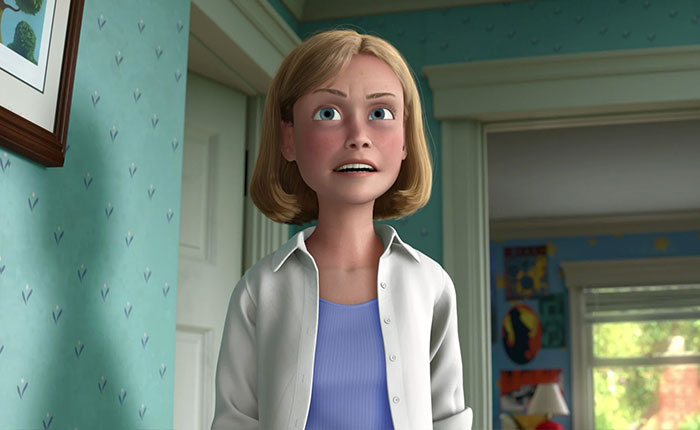 Andy&rsquo;s mom from Toy Story standing in a blue room with wallpaper, wearing a white shirt and a blue top.