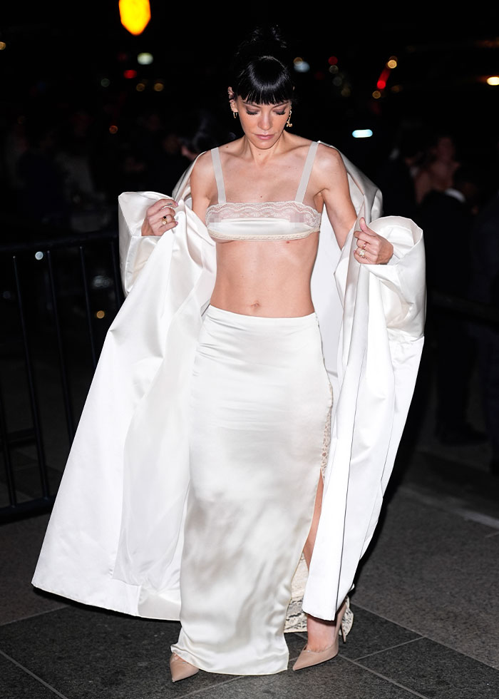 Woman in a sheer white crop top and skirt with a long coat, showcasing a bold celebrity fashion disaster in 2025.