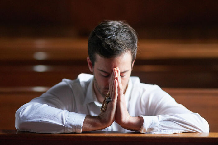 Man sitting in church pew praying with rosary beads, symbolizing crazy things people have done believing their ex will pine.