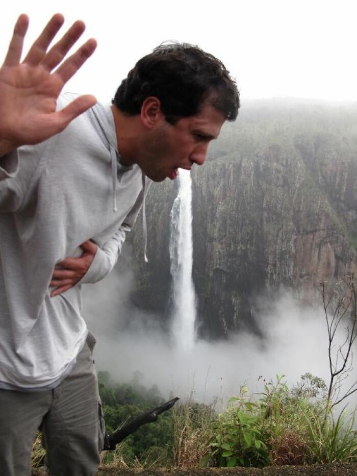 Man in a grey hoodie pretending to vomit a waterfall in a trippy picture that seems plucked from another reality.