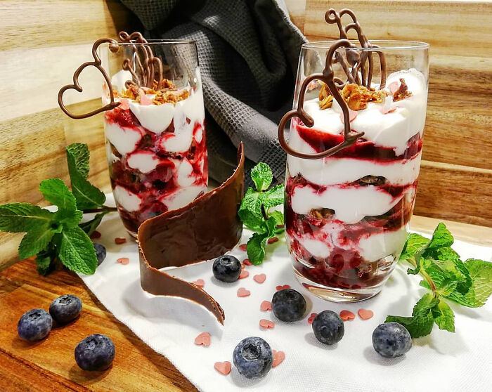 Christmas desserts featuring layered cream and berry parfaits garnished with chocolate hearts and fresh blueberries.
