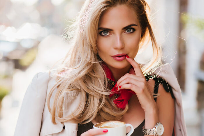 Blonde woman with intense gaze holding coffee cup, hinting at dark secrets and hidden emotions in natural light setting.