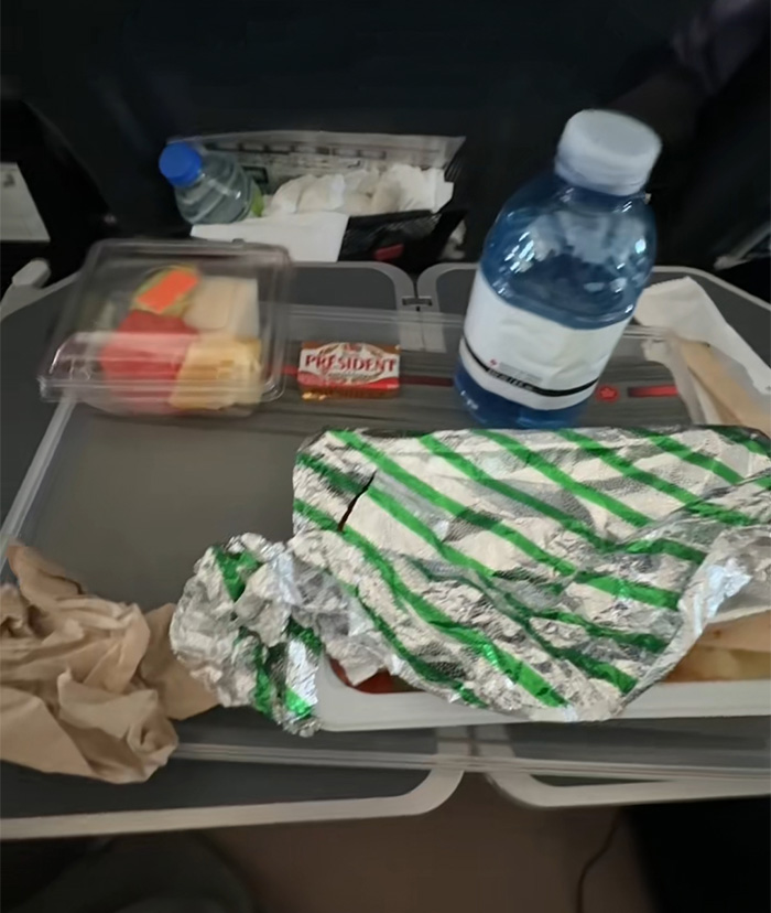 Comida servida en vuelo de Air Canada con agua y alimentos empaquetados en bandeja durante cr&iacute;tica de pasajera.