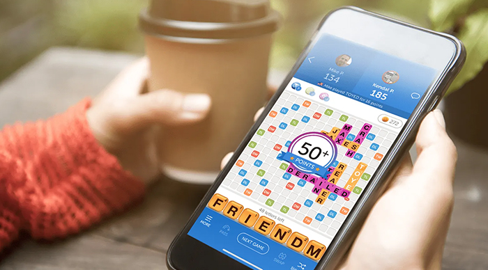 Person holding smartphone showing a digital word puzzle, demonstrating the best party game with vibrant colors and scores.