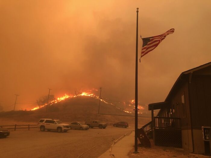 Wildfire blazing on a hill near vehicles and a flagpole, capturing moments when people instinctively felt something was wrong.