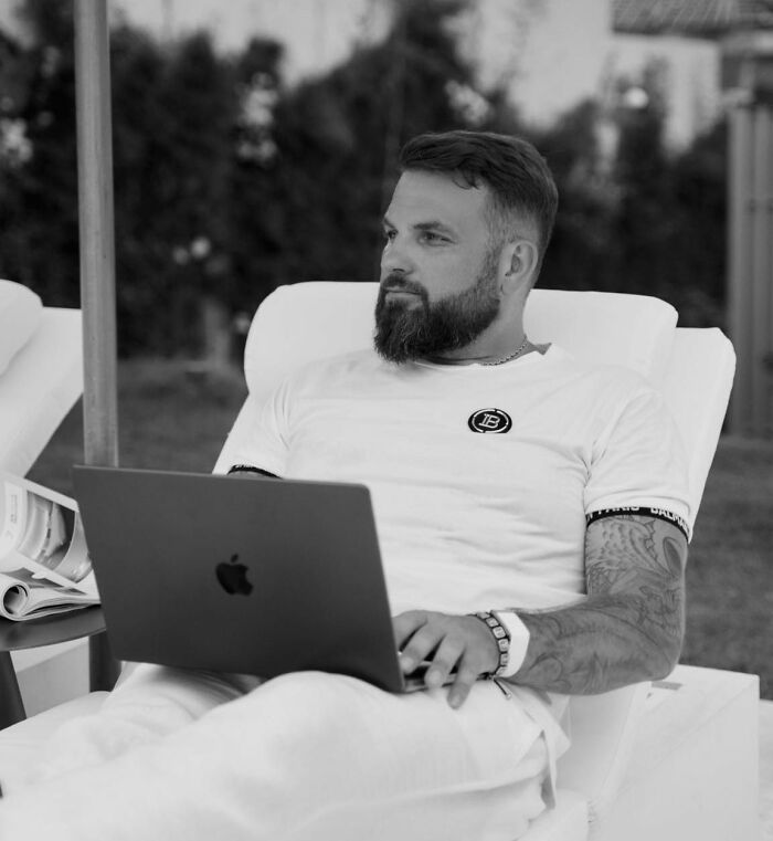 Man with beard and tattoos using a laptop outdoors, related to crypto scammer case in Dubai mall investigation. Man with beard and tattoos using a laptop outdoors, related to crypto scammer case in Dubai mall investigation.
