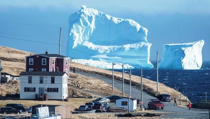 Massive iceberg near a coastal town with people observing, illustrating existence and reality in the universe.