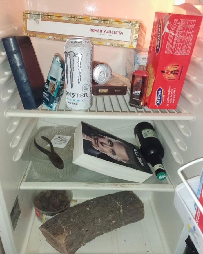Fridge stocked with unusual items including a book, log, energy drink, and cigar box in a dude fridge setting.