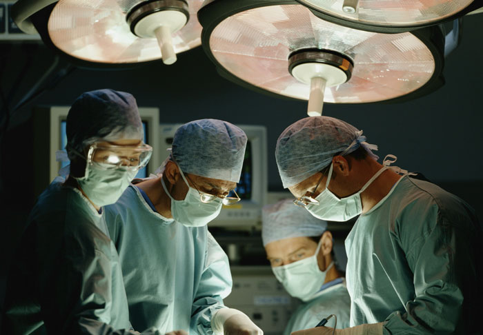 Surgeons performing a complex operation under bright surgical lights in a sterile operating room environment.