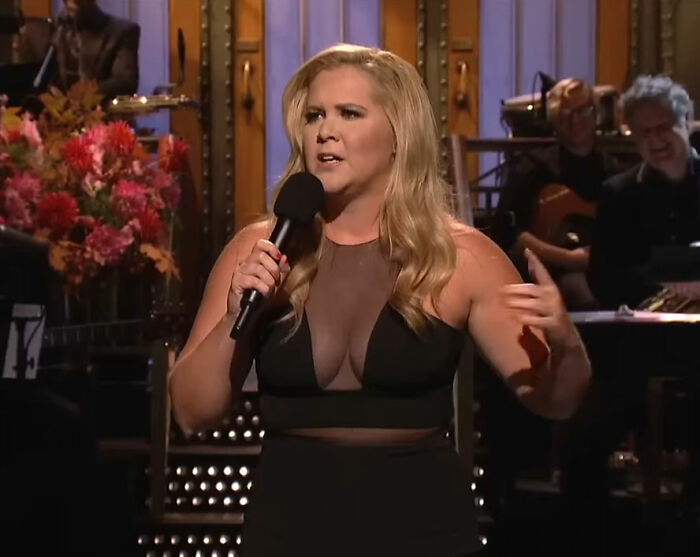 Amy Schumer performing on stage, holding a microphone and showcasing dramatic weight loss during a live comedy show.