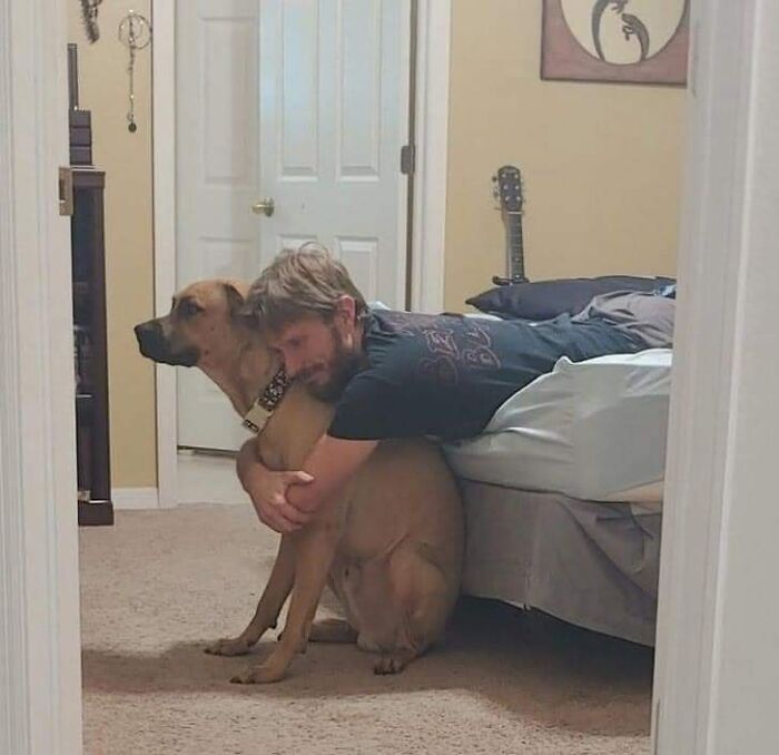 Man lying on bed hugging a dog sitting on the floor in a cozy room, capturing hilarious moments caught on camera.