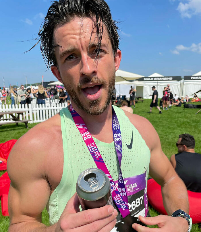 David Corenswet at outdoor event wearing race bib and medal, holding a drink, showcasing modern masculinity.