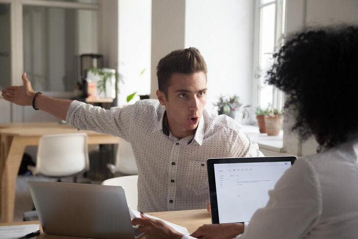 Two coworkers talking and using laptops in an office, sharing small tricks that make being a grown-up easier