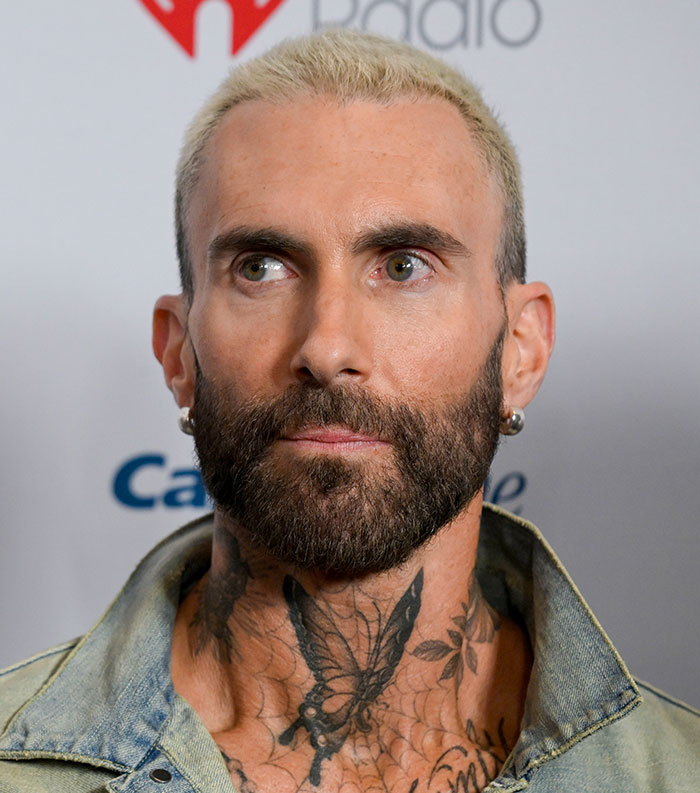 Man with blonde hair, beard, earrings, and butterfly neck tattoo at a radio event, one of the most disliked stars this year.