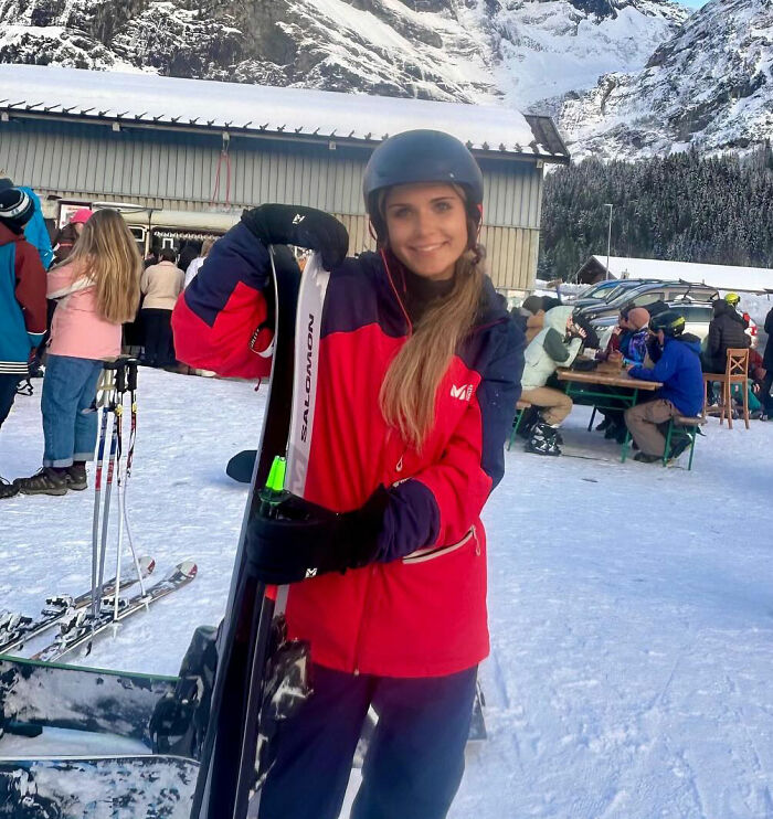Young woman in ski gear holding skis outdoors at snowy mountain resort, related to sorority girl tragic accident news.