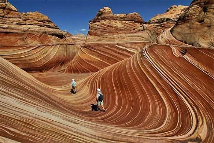 Two hikers exploring wave-like rock formations in a real place that looks AI generated from around the world.