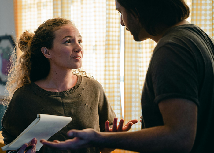 Woman hosting casual Christmas talks with man while dealing with toxic mother-in-law conflict indoors near window light.