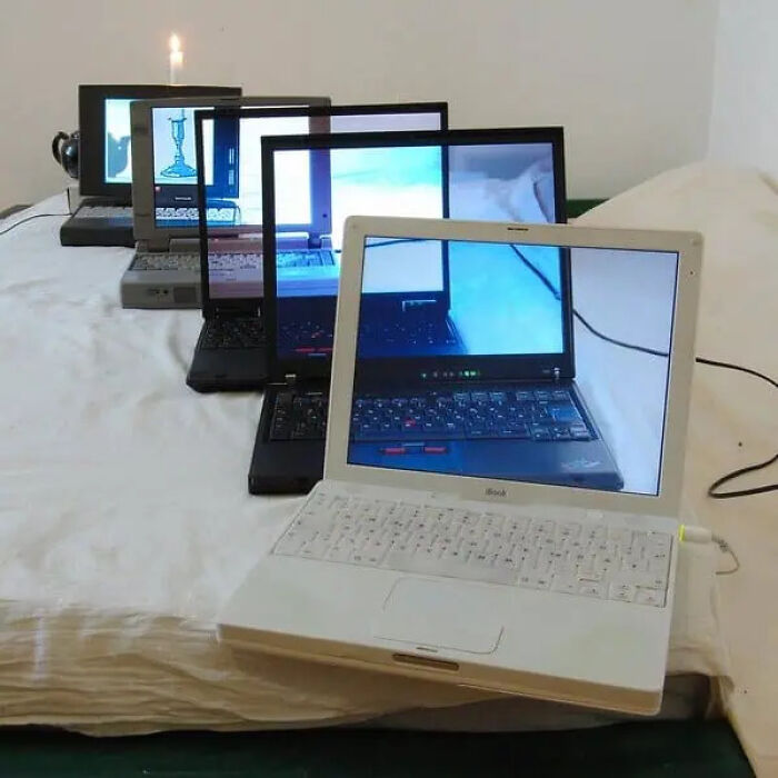 Array of vintage laptops on a bed displaying recursive trippy pictures that create a surreal, otherworldly effect.