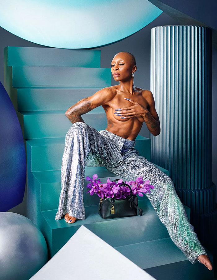 Cynthia Erivo posing topless on teal stairs with silver pants and a handbag filled with purple flowers in artistic setting Cynthia Erivo posing topless on teal stairs with silver pants and a handbag filled with purple flowers in artistic setting