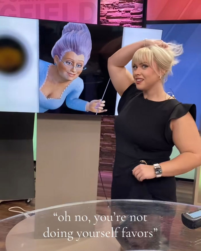 Curvy news anchor in black dress reading mean viewer comments during broadcast with animated character on screen.
