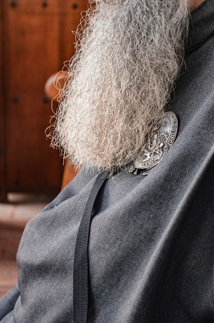 Close-up of a person with a long gray beard wearing a medallion on dark fabric, sparking people to question what they saw.