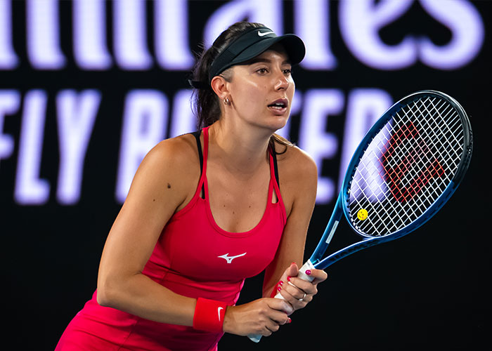 Female tennis player in red outfit preparing to return a serve during a professional match, highlighting tennis star career transition.