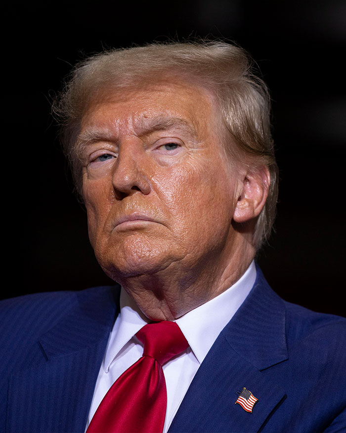 Donald Trump in a blue suit and red tie, facing forward with a serious expression during a public appearance. Donald Trump in a blue suit and red tie, facing forward with a serious expression during a public appearance.