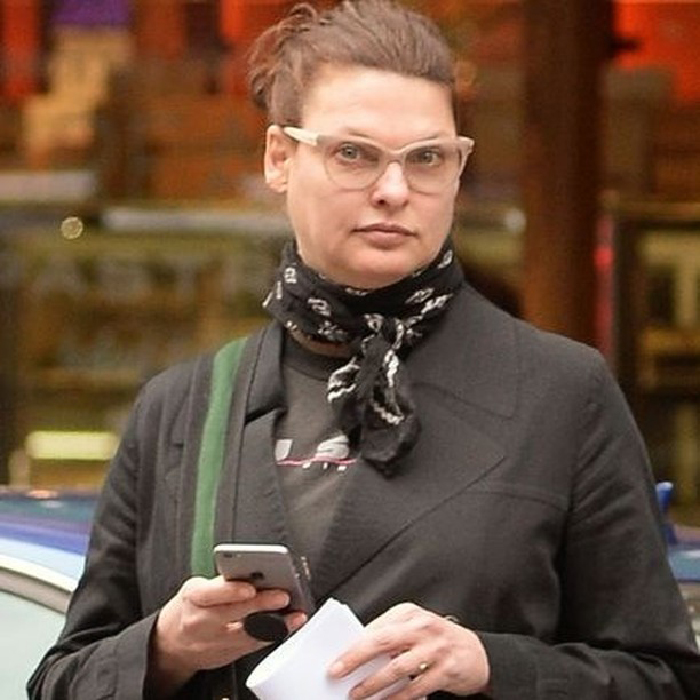 Linda Evangelista outdoors wearing glasses and a black scarf, holding a phone, related to Coolsculpting photos and story.