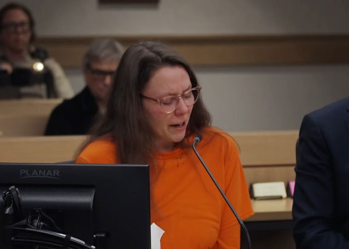 Woman in orange shirt sobbing at a courtroom microphone, engaged teacher learning her fate in a disturbing case.
