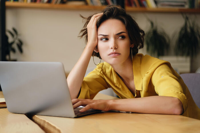 Young woman in yellow shirt looking frustrated while using laptop, illustrating family drama without intention concept
