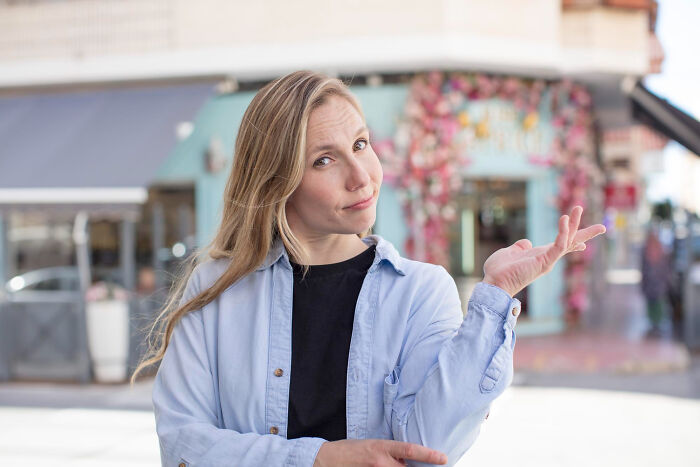 Young woman in a casual outfit smiling and gesturing outdoors, illustrating small tricks to make being a grown-up easier.