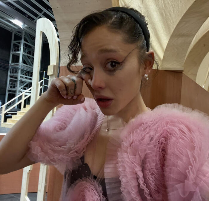 Young woman in a pink ruffled dress wiping tears, conveying emotional struggles related to Ariana Grande's family and singer challenges.