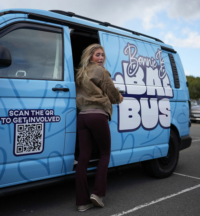 Woman standing by a blue Bonnie Blue bus with QR code, symbolizing Bonnie Blue learning her fate after controversial video arrest.