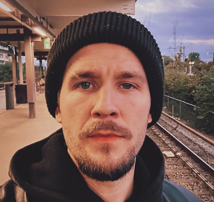 Close-up of Tylor Chase wearing a black beanie at a train station, highlighting his homelessness and urgent support request.