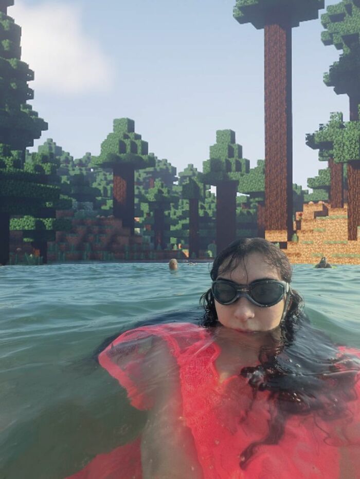 Person wearing goggles and a red top swimming in water with a background of trippy pixelated blocky trees and landscape.