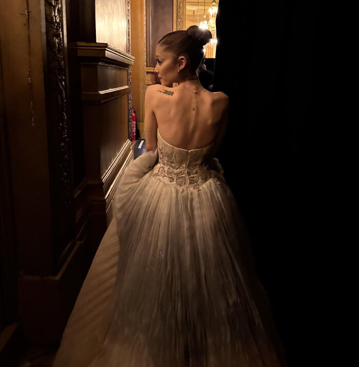 Ariana Grande in a strapless gown, backstage in dim lighting, highlighting struggles shared by family member.