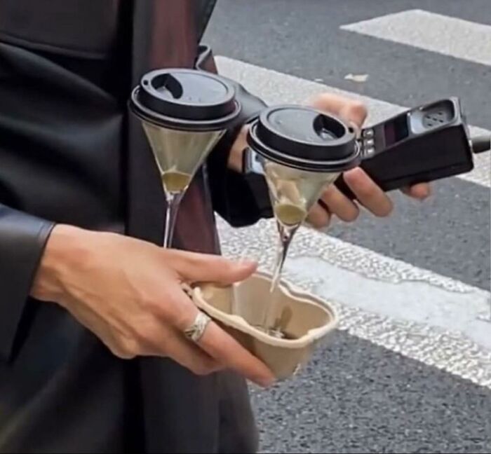 Person holding two upside-down martini glasses with coffee cup lids and a cardboard drink holder in a trippy picture.