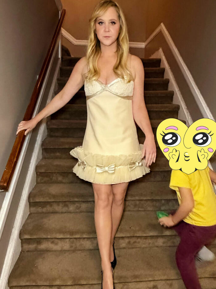 Amy Schumer showing off dramatic weight loss in a cream dress, standing on carpeted stairs with a child nearby.
