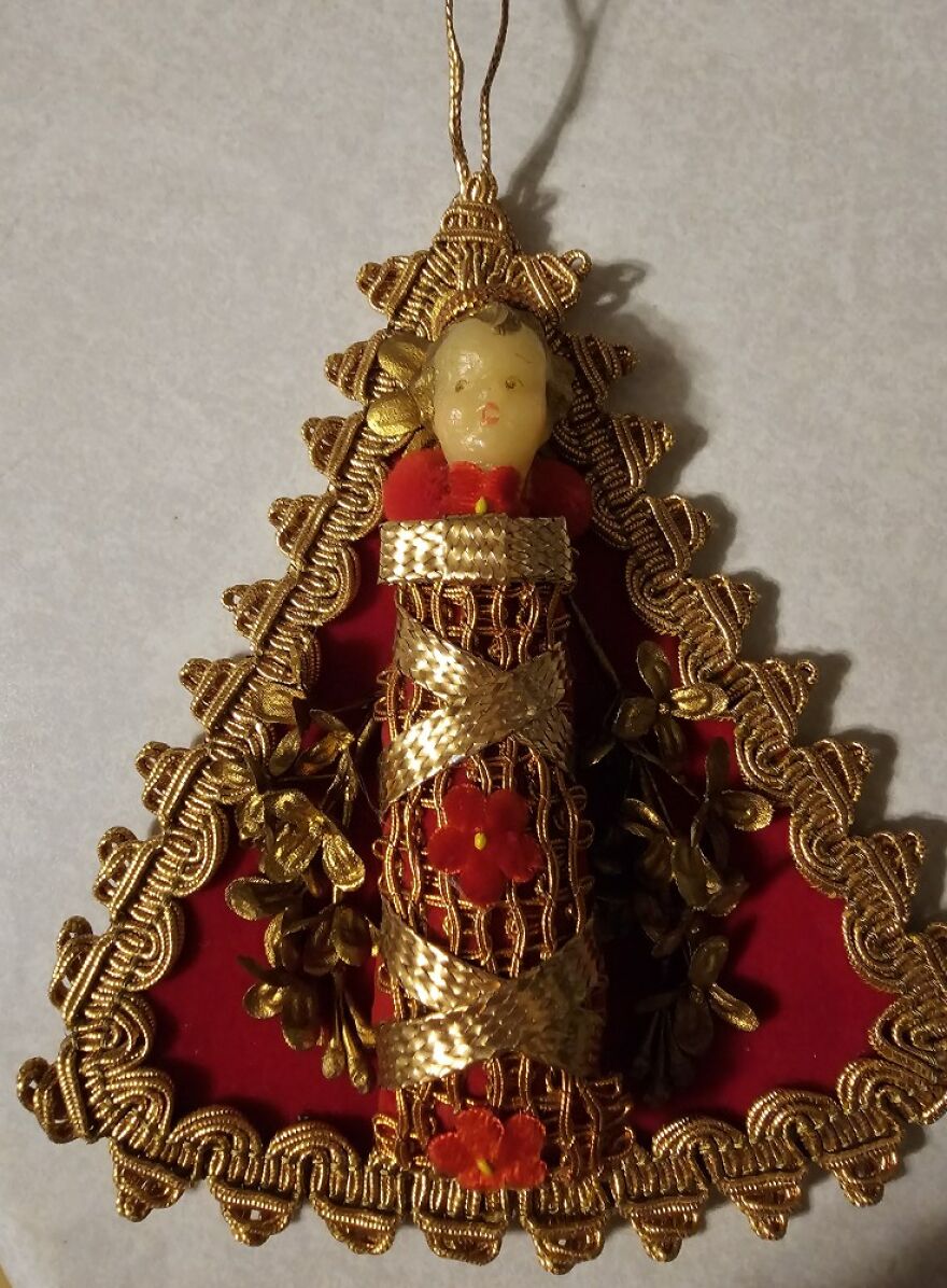 Vintage Christmas decoration ornament featuring a small figure wrapped in gold ribbons and red flowers with gold trim.