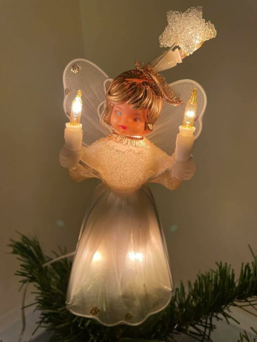Vintage Christmas decoration angel tree topper with glowing lights and translucent wings on a green pine branch.