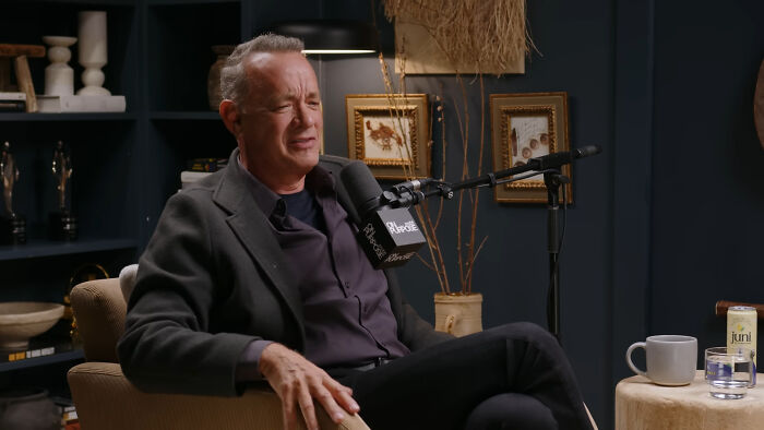 Actor in a podcast studio sharing fascinating secrets about celebrities with a microphone and casual setup around him.