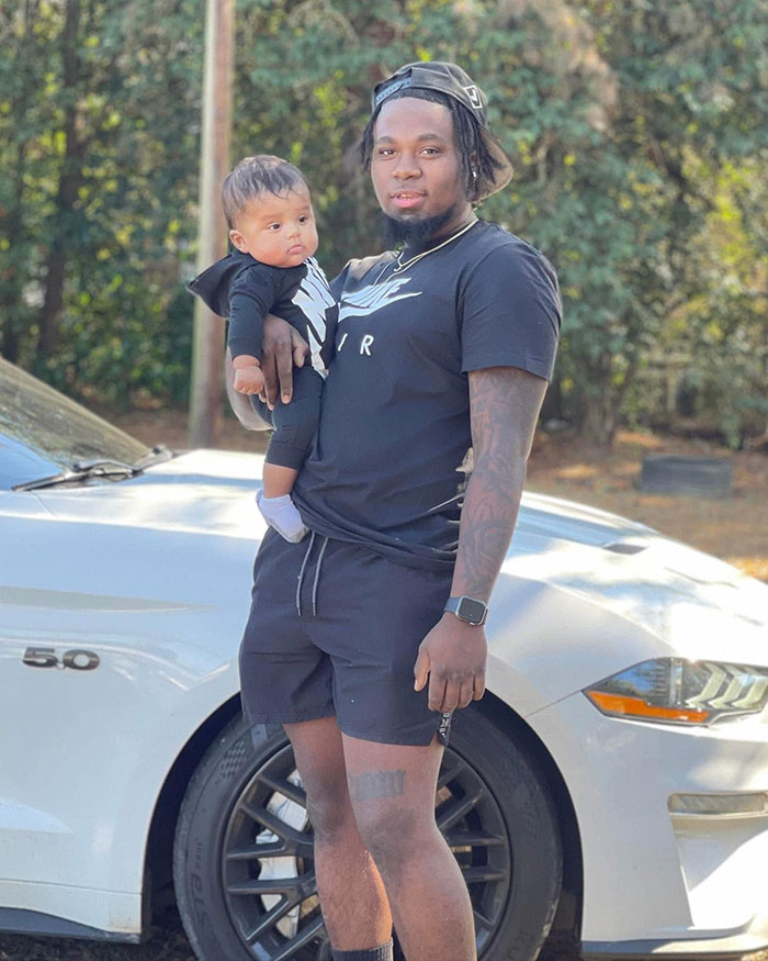 Man holding toddler outdoors near white car, unrelated to beauty queen accused in toddler&rsquo;s passing court case.