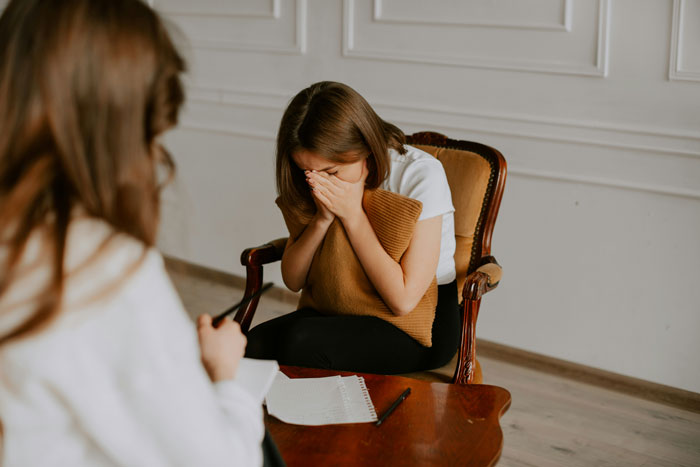 Couple in therapy session, woman upset and hugging pillow, discussing forgiveness challenges and relationship struggles.