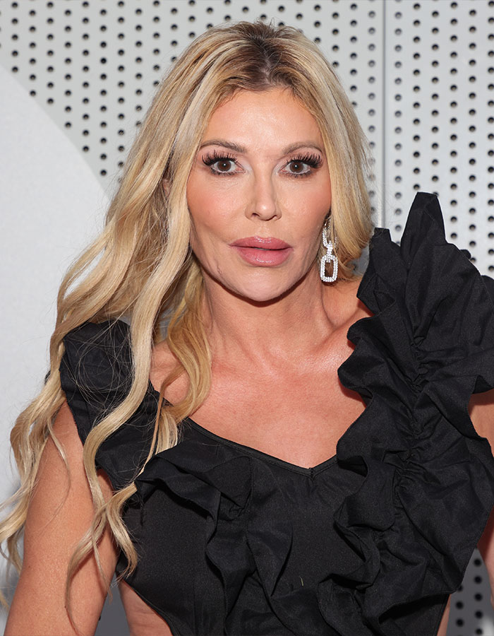Brandi Glanville wearing a black ruffle dress and statement earrings posing against a dotted white background.
