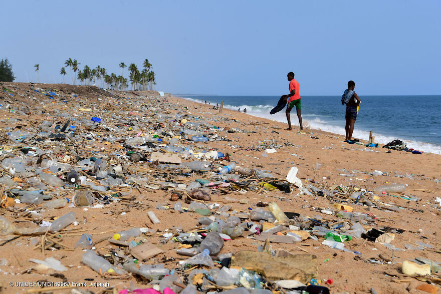Beach covered in plastic waste and pollution with two people standing near the water, illustrating dirtiest countries pollution impact.