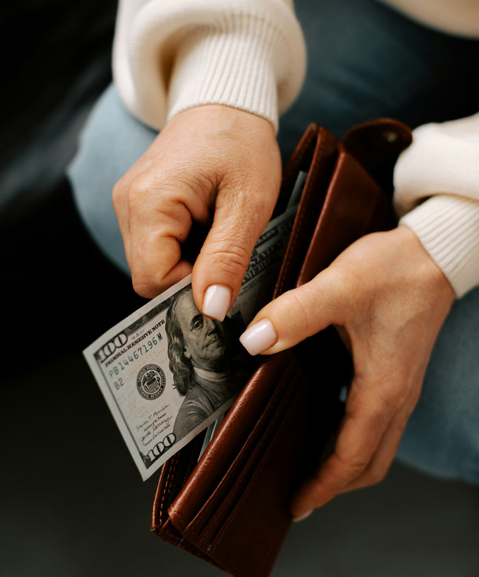 Close-up of hands holding a wallet with cash, illustrating people terrified of these next-level evil kids they know.