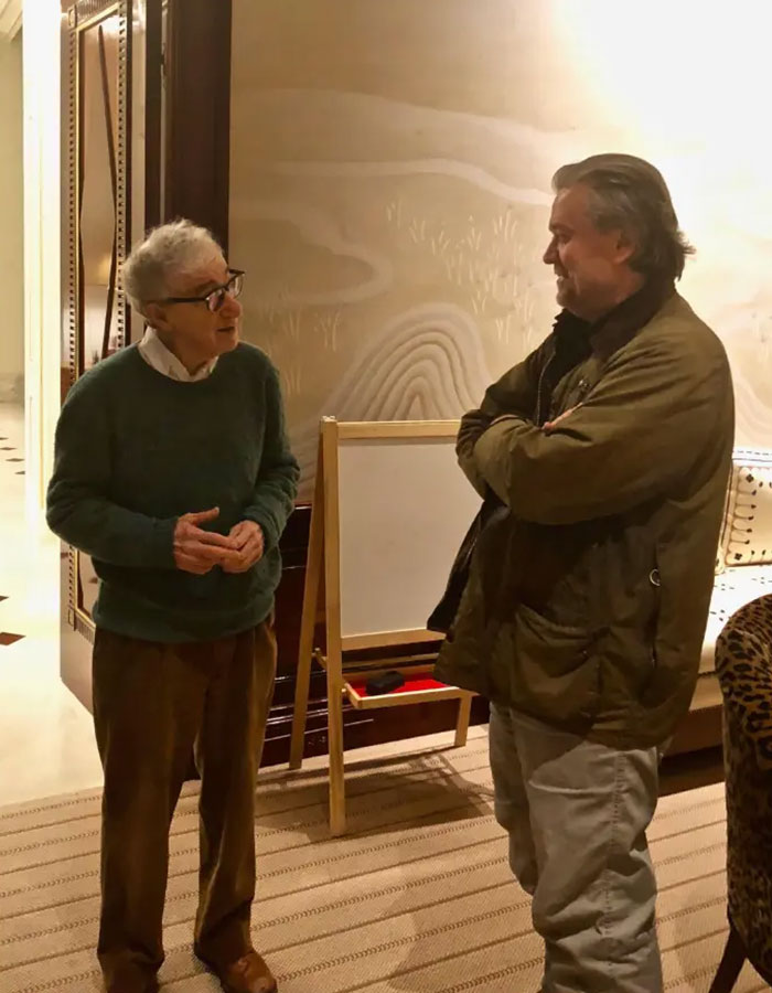 Two men conversing indoors near a wooden easel, with a focus on disturbing Epstein desk photo after estate images release. Two men conversing indoors near a wooden easel, with a focus on disturbing Epstein desk photo after estate images release.