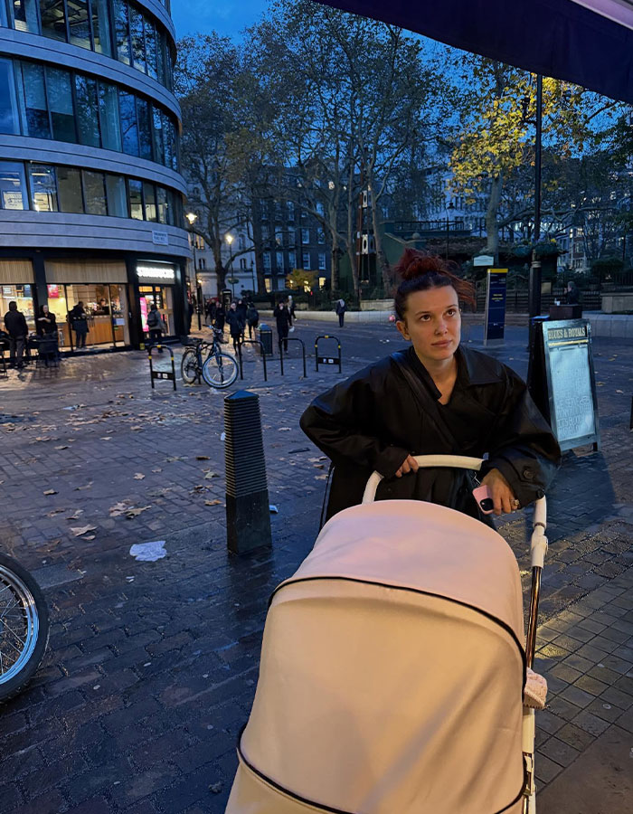 Millie Bobby Brown pushing a stroller outdoors at dusk, showing an arm injury that fuels fan theories about Jake Bongiovi control.