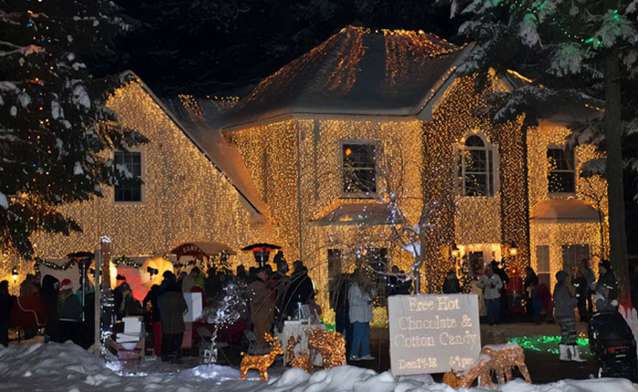 House covered in Christmas lights with people gathered outside in snow, featuring viral Christmas lawyer holiday display.