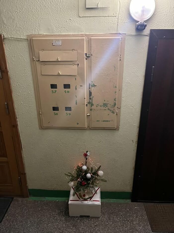 Small, quirky Christmas decoration with lights and ornaments in a dull Lithuanian apartment building hallway.